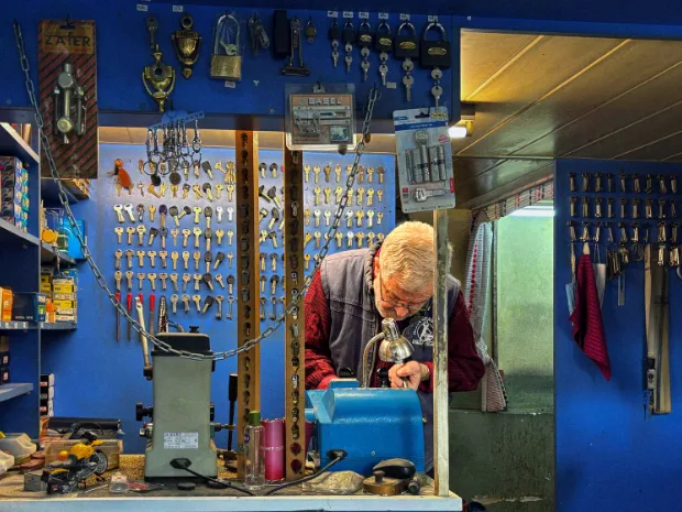 Cerrajero haciendo una copia de llave en el taller, con la pared llena de llaves colgadas