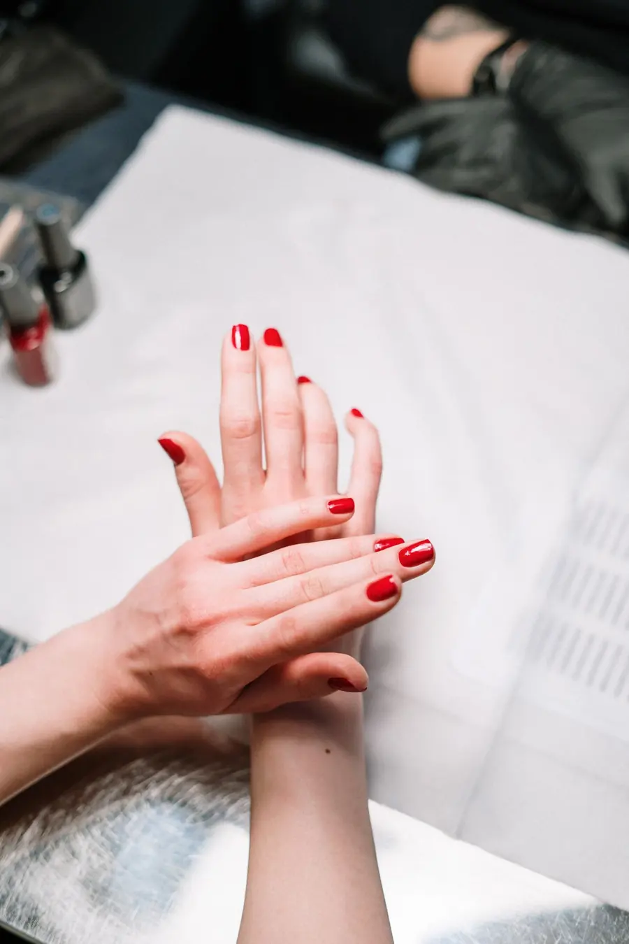 Unas manos con las uñas pintadas de rojo apoyadas sobre una toalla blanca.