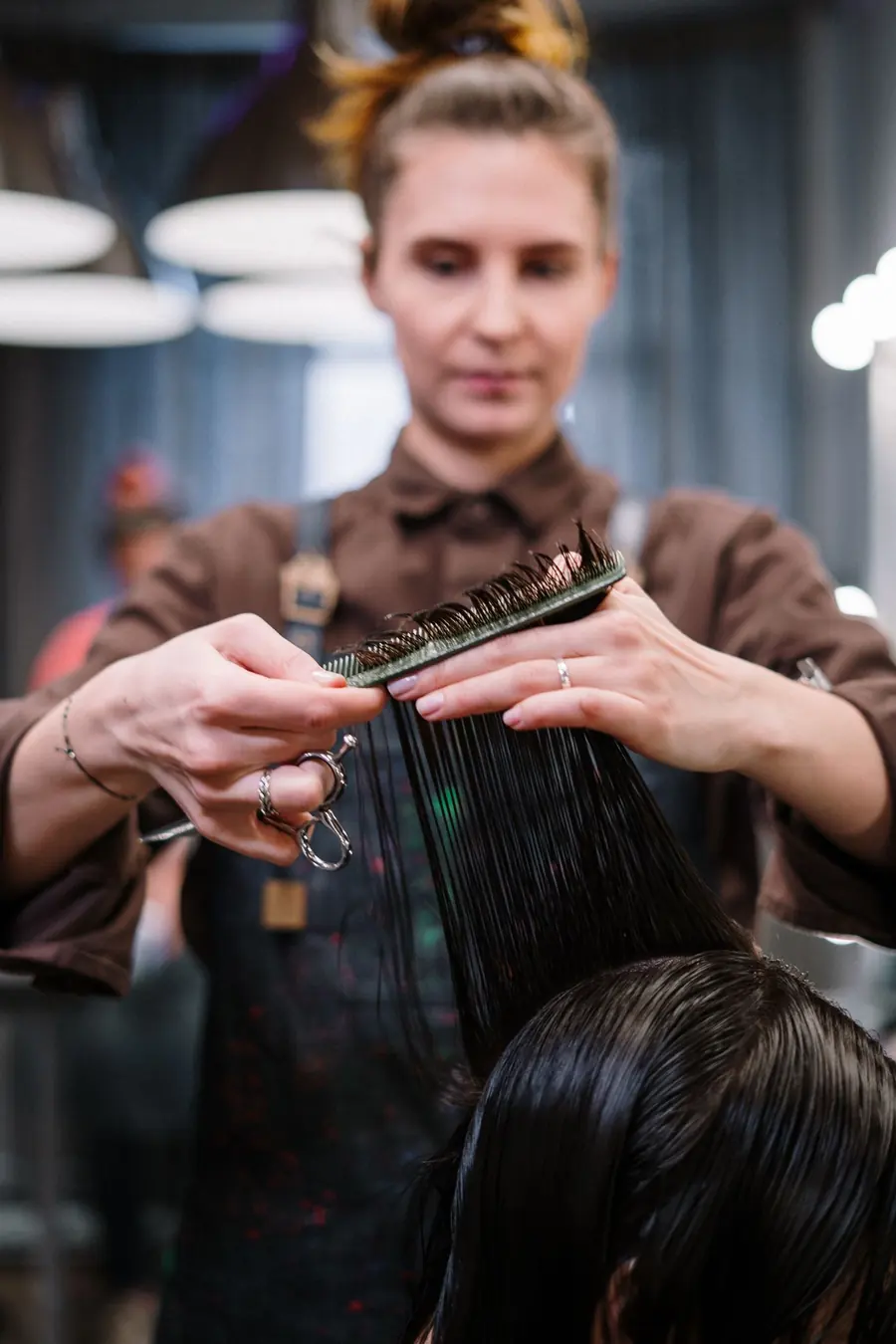 Una peluquera corta a tijera un mechón de pelo mojado sujeto con el peine.