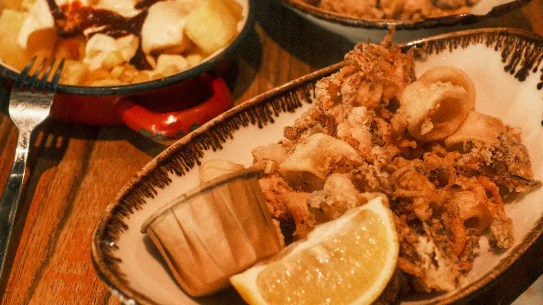 Fuente de calamares con limón y una cazuela de bravas en una mesa de barril
