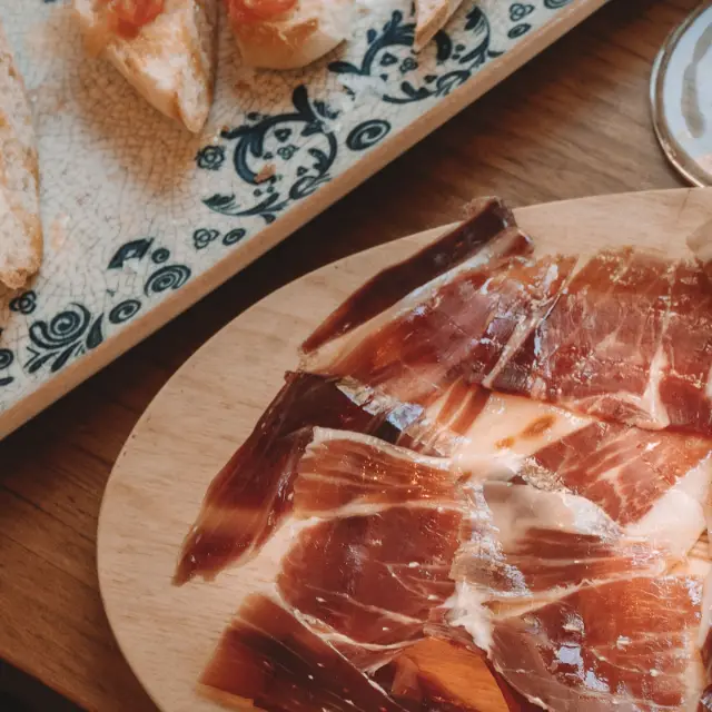 Jamón cortado a cuchillo en tabla de madera y pan con tomate en plato de azulejo